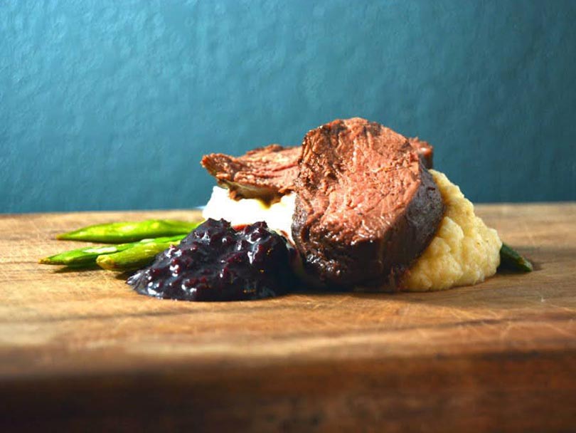closeup of sous vide steak with blueberry sauce and asparagus
