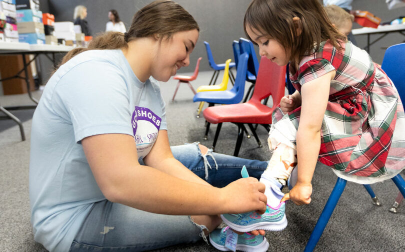 Share the Spirit volunteer Gracieana Smith helps a preschooler try on new shoes at a pop-up shoe giveaway event in Limon.