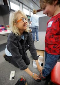 Share the Spirit co-founder Karen Voepel shares a smile with a little boy while helping him try on a pair of new shoes at a preschool shoe giveaway event.